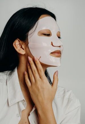 An Asian woman gently applies a face mask as part of her skincare routine, focusing on beauty and self-care.
